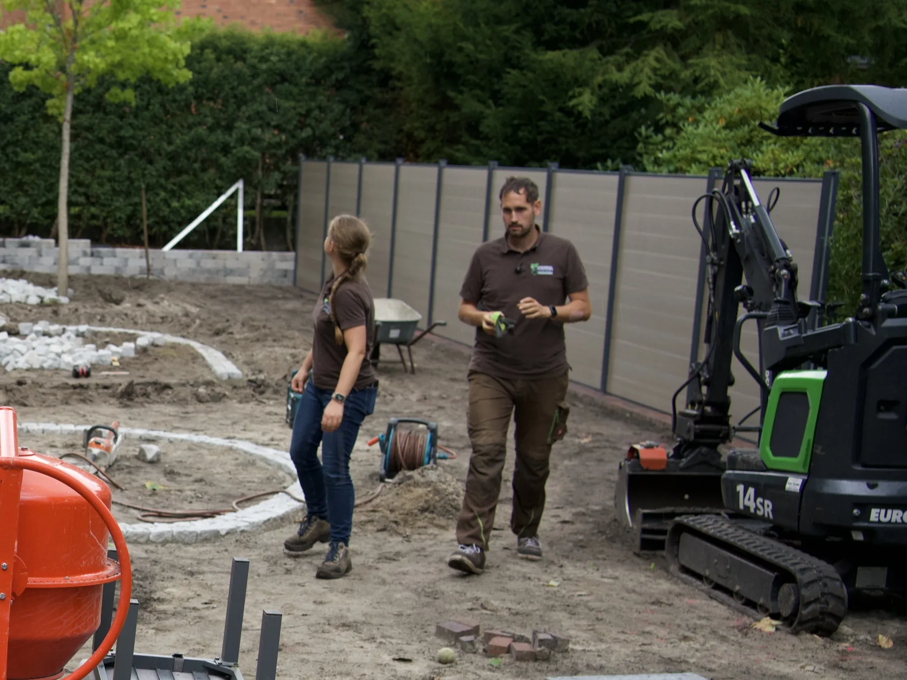 Eric Herrmann-Meiser mit einer Kollegin auf einer Gartenbaustelle in Oldenburg, daneben der Minibagger
